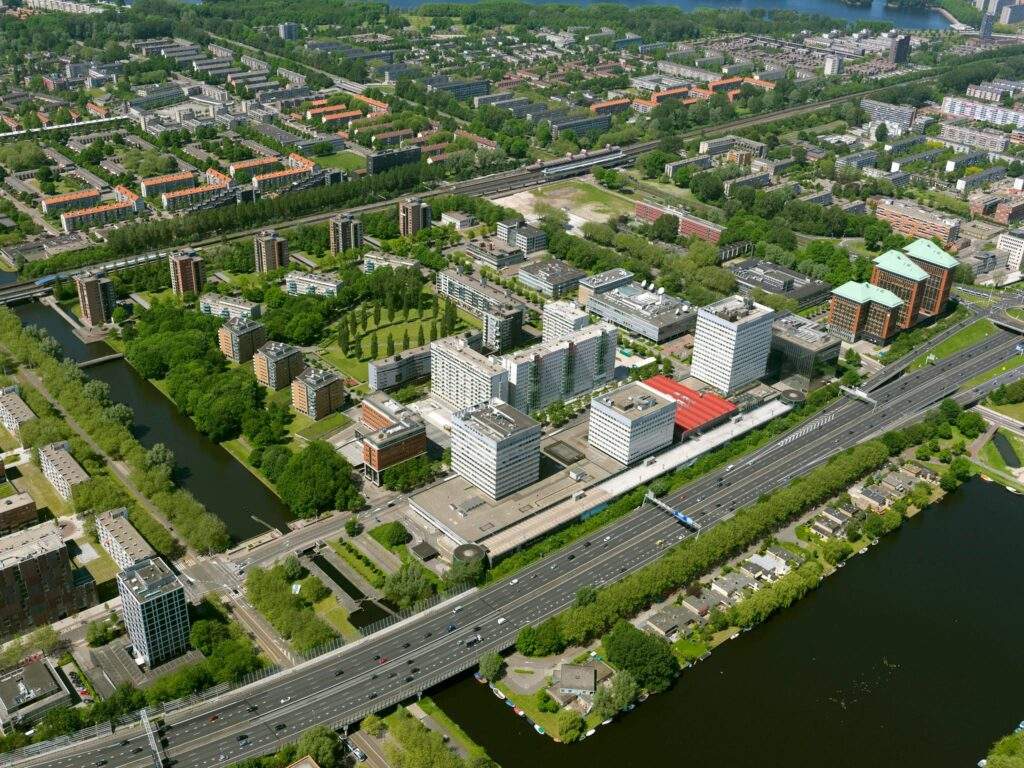 Luchtfoto van het Koningin Wilhelminaplein in Amsterdam met omliggende kantoren, woonwijken en snelweg.